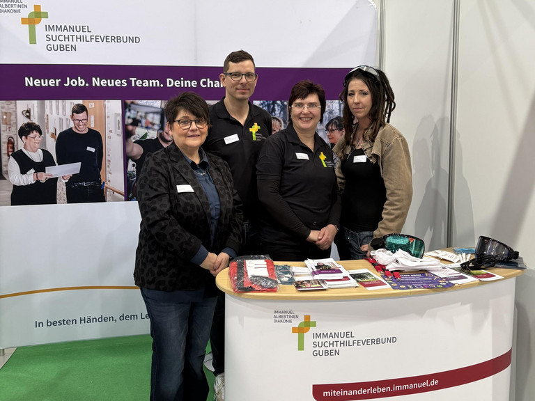 Marion Swietza, Doreen Lindner, Steffi Mattke und Christopher Betz vom Immanuel Suchthilfeverbund Guben stehen an dem mit Logos und Bannern gestalteten Messestand vor einem Tisch mit Informationsmaterialen und Giveaways auf der Ausbildungsmesse Impuls in Cottbus und blicken in die Kamera Marion Swietza, Doreen Lindner, Steffi Mattke und Christopher Betz vom Immanuel Suchthilfeverbund Guben stehen an dem mit Logos und Bannern gestalteten Messestand vor einem Tisch mit Informationsmaterialen und Giveaways auf der Ausbildungsmesse Impuls in Cottbus und blicken in die Kamera